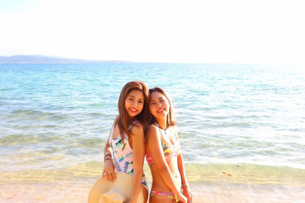 星砂海岸の青い海をバックに写真撮影をする水着姿の女性2人